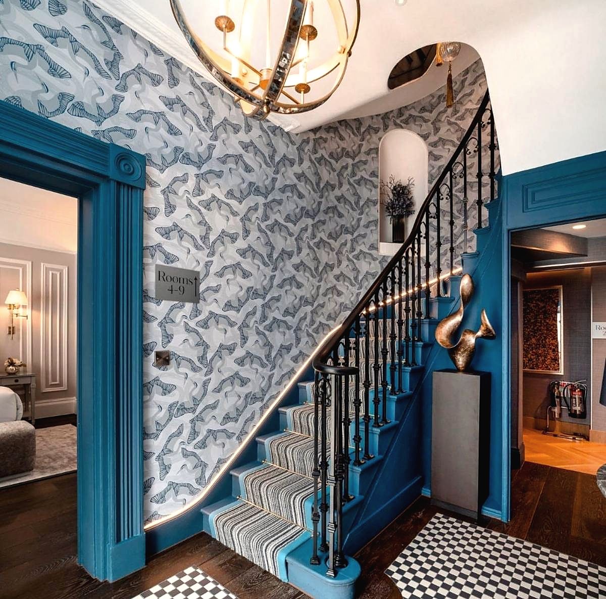 Staircase with blue painted joinery, patterned wallpaper and a brass orb pendant