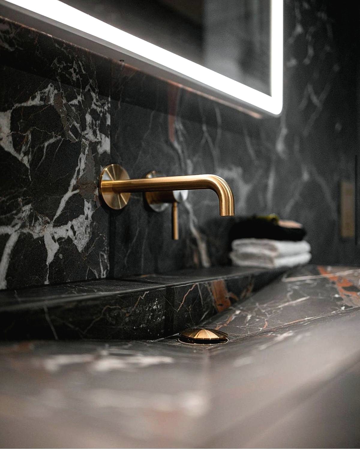 Close detail of a brass wall mounted tap against dark marble